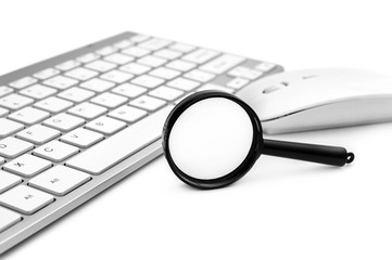 Magnifying glass with computer keyboard and mouse on white.