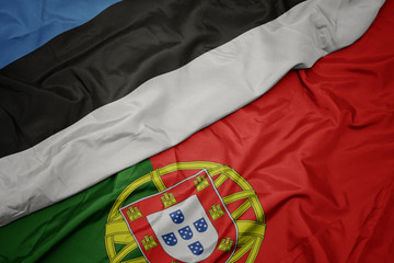 waving colorful flag of portugal and national flag of estonia.