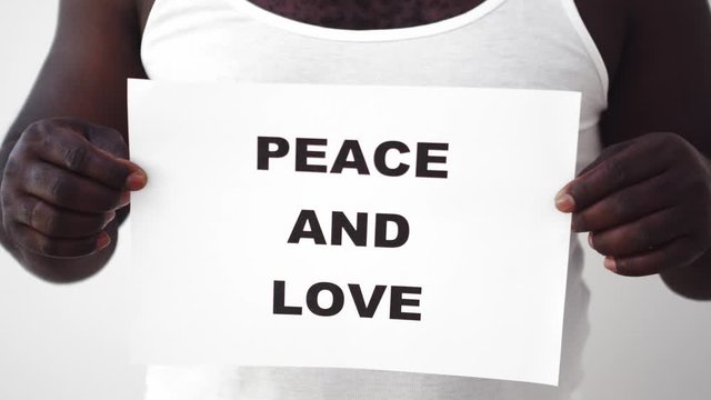 Black man in white T-shirt raises a sign "Peace and Love". Protest sign, medium shot.