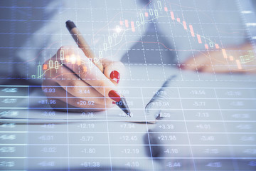 Double exposure of woman's hands making notes with forex graph hologram. Concept stock market...