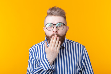 Young man with a mustache and beard making bulging eyes in surprise against a yellow background. Concept of surprise and uncertainty.