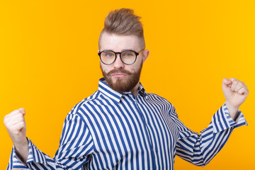 People, emotions and victory concept - Funny young man dressed in shirt showing fists up over yellow background