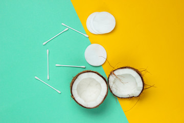 Minimalistic natural beauty concept. Coconut halves, cosmetic accessories on a blue-yellow pastel background. Top view