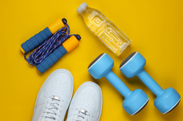 Naklejka na ściany i meble Flat lay style sport concept. Dumbbells, sneakers, jump rope, bottle of water. Sports equipment on yellow background. Top view