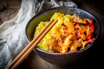 Saffron rice with pieces of chicken and vegetables on wooden table.