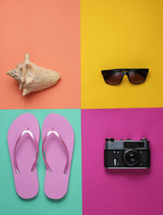 Obraz premium Summer still life. Beach accessories. Fashionable pink flip flops, retro camera, seashell, sunglasses on colored paper background. Flat lay. Top view. Minimalism