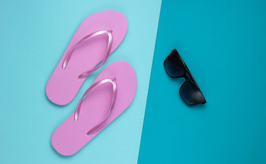 Summer still life. Beach accessories. Fashionable beach pink flip flops, sunglasses on blue  paper background. Flat lay. Top view