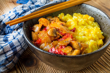 Saffron rice with pieces of chicken and vegetables on wooden table.