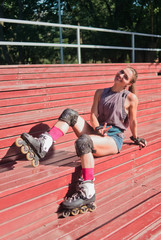 Cheerful sporty woman roller skating in roller skates sitting on a wooden tribune on the sports...