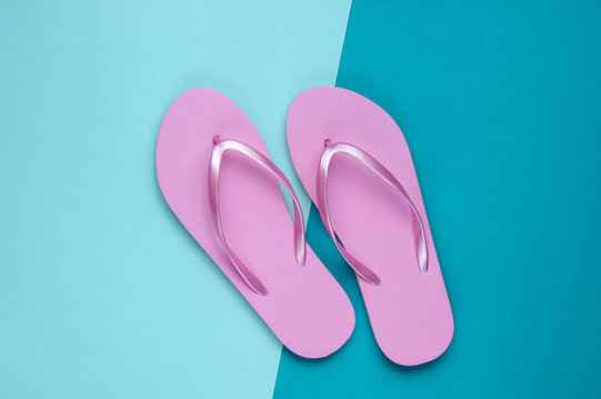 Fashionable beach pink flip flops on blue paper background. Top view