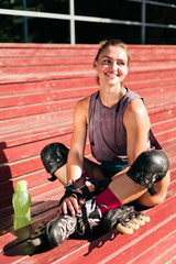 Cheerful sporty woman roller skating in roller skates sitting on a wooden tribune on the sports...
