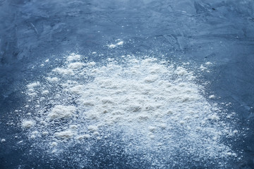 Fototapeta premium Side view of a pile of sprinkled baking white flour with shallow depth of field on a textured blue table with empty space for text