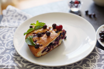 Piece of pie with blueberries, rasberry and mint for dessert on a white plate, napkin. Pieces of delicious homemade cake