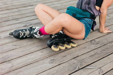Woman roller skater sitting wooden boards outdoors. Crop photo legs.  Sport lifestyle