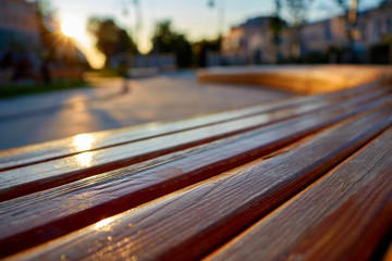 Curved wooden bench in the rays of the rising sun and a blurred background. Bench in the city square at dawn.