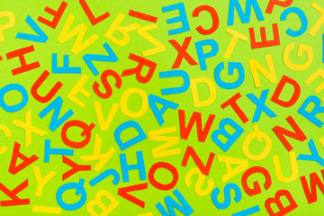 Multicolored letters of the English alphabet cut out of cardboard laid out randomly on a green background