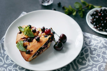 Piece of pie with blueberries, rasberry,cherries and mint for dessert on a white plate, napkin. Pieces of delicious homemade cake