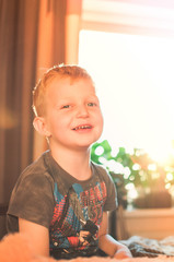 Portrait of a cute 5 year old boy in a room at sunset day in the backlight. The face of a happy child and a smile.