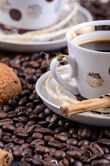 white coffee mug on a saucer on a stone table with scattered coffee beans, oatmeal cookies and cinnamon stick
