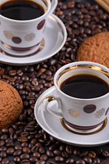 white coffee mug on a saucer on a stone table with scattered coffee beans, oatmeal cookies, chocolate and cinnamon stick