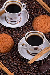white coffee mug on a saucer on a stone table with scattered coffee beans, oatmeal cookies, chocolate and cinnamon stick
