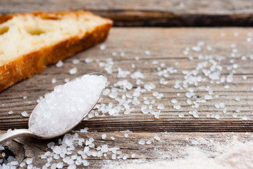 salt crystals on old spoon, slice of bread on old wooden