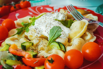 Dumpling on a plate with tomatoes and spinach leaves.
