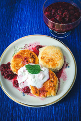 cheesecakes with raspberry jam and sour cream on a plate on blue backround