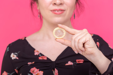 Safe sex, health and contraception concept - a condom in woman's hands close up on pink background