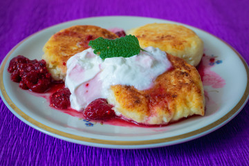 cheesecakes with raspberry jam and sour cream on a plate on purple backround