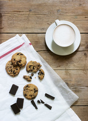Chocolate cookies, pieces of chocolate and a cup of cocoa or coffee with milk on a wooden background. Rustic style.