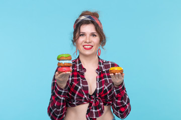Positive young pin-up girl model holding in hands four multicolored donuts posing on a blue...