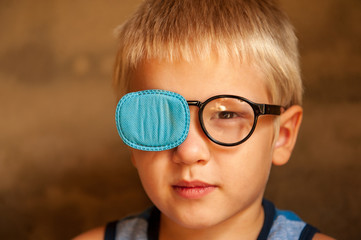 Portrait of funny child in new glasses with patch for correcting squint .Ortopad Boys Eye Patches...