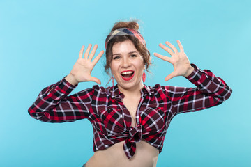 Beautiful cheerful young pin-up girl posing in a plaid shirt and bandage against a blue background....