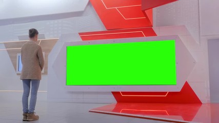 Woman looking at blank large interactive wall green display at modern technology exhibition or museum with futuristic sci-fi interior. Mock up, green screen, template, education, chroma key concept