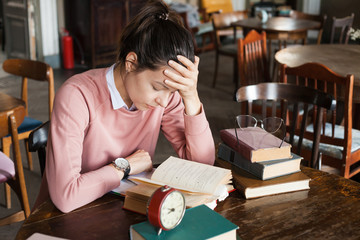 Lack of sleep. Student girl, brunette, bent over books at a table in an old library, supporting her head with her hand.