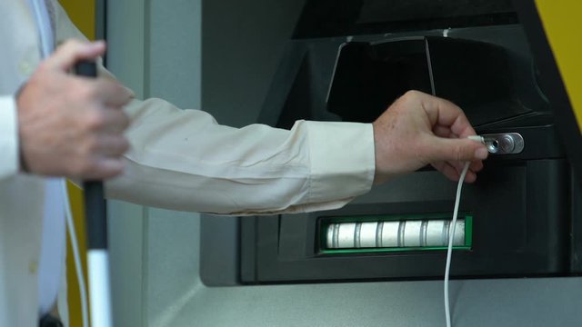 Blind senior man trying to connect headphones to atm to withdraw cash, banking