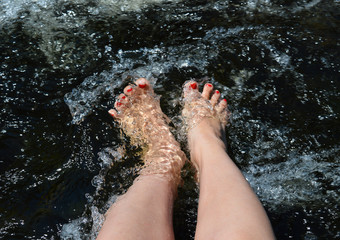 A pair of feet with red-painted toenails splash in the rushing water of the river.