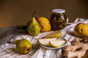 The photo shows fresh pears, a jar of jam and ginger root on the background of the tablecloth.