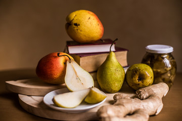 The photo shows fresh pears, a jar of jam and ginger root on the background of the tablecloth.