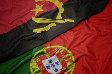 waving colorful flag of portugal and national flag of angola.