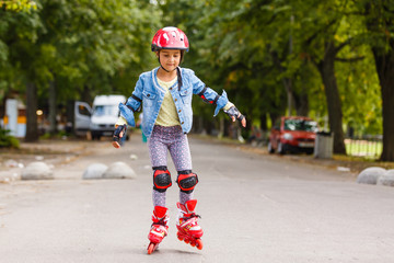 Funny Little pretty girl on roller skates in helmet riding in a park. Healthy lifestyle concept.