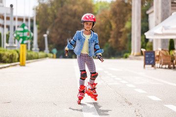 Funny Little pretty girl on roller skates in helmet riding in a park. Healthy lifestyle concept.