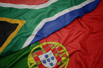waving colorful flag of portugal and national flag of south africa.