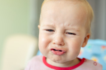 Cute adorable caucasian blond toddler boy sitting in high chair and crying while feeding. Upset unhappy child refuse to eat healthy diet food and demanding bad unhealthy fastfood meals