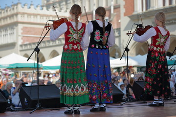 Female band on stage, three young Polish girls play violin, dressed in beautiful colorful...
