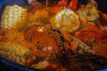 Obraz na płótnie Canvas Closeup of Steaming hot blue pot of Cajun Seafood boil, including crab shrimp crawfish corn potatoes lemon andouille sausage in a spicy broth