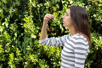 Health and medicine - Young woman sneezing in the woods with a handkerchief.