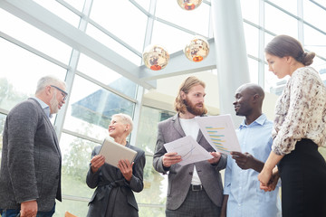 Waist up portrait of diverse group of business people standing in hall of modern office building discussing work, copy space