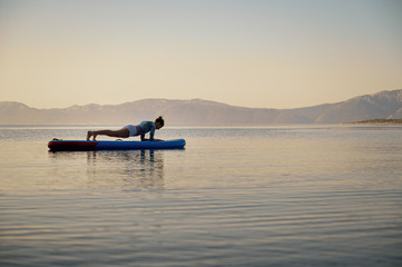 Young woman making plank workout on a stand up paddle board